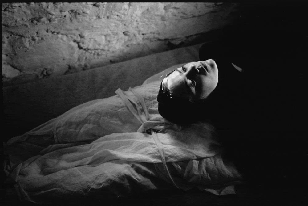 A woman (Emma Stone) wearing a black headscarf lies on a shrouded body. A bare-chested man (Damien Bonnard) stands in a doorway. Scenes from a film shot by Yorgos Lanthimos.